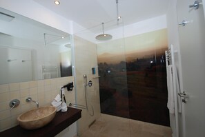 Un baño moderno con ducha de vidrio, un espejo grande y un lavamanos color beige.