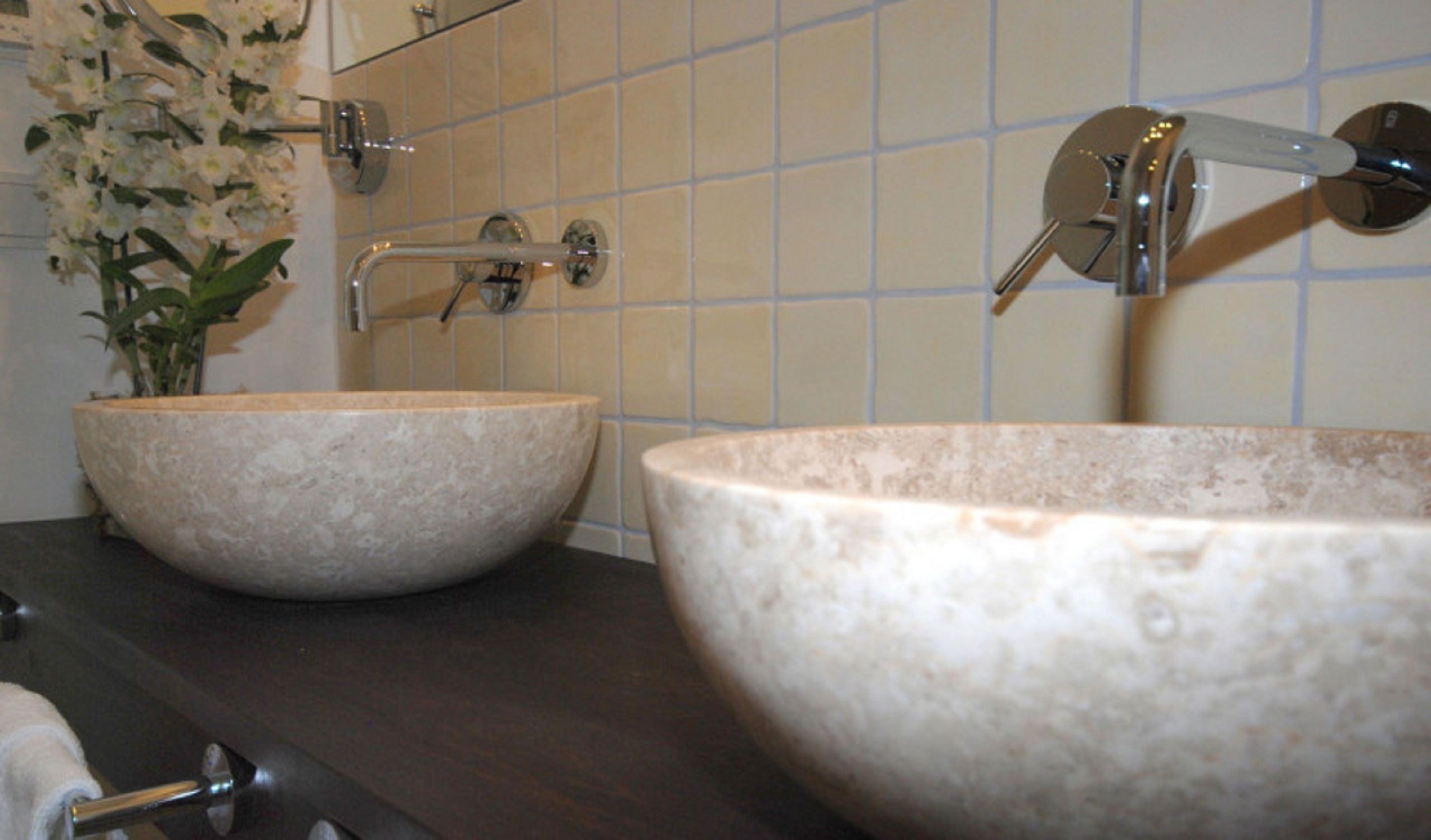 Two large, round, beige stone sinks with a modern faucet and a mirror above them.