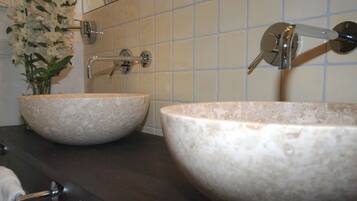 Two large, round, beige stone sinks with a modern faucet and a mirror above them.