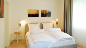 Een hotelkamer met een bed, twee wandlampen, een klein rond tafeltje en twee schilderijen aan de muur.
