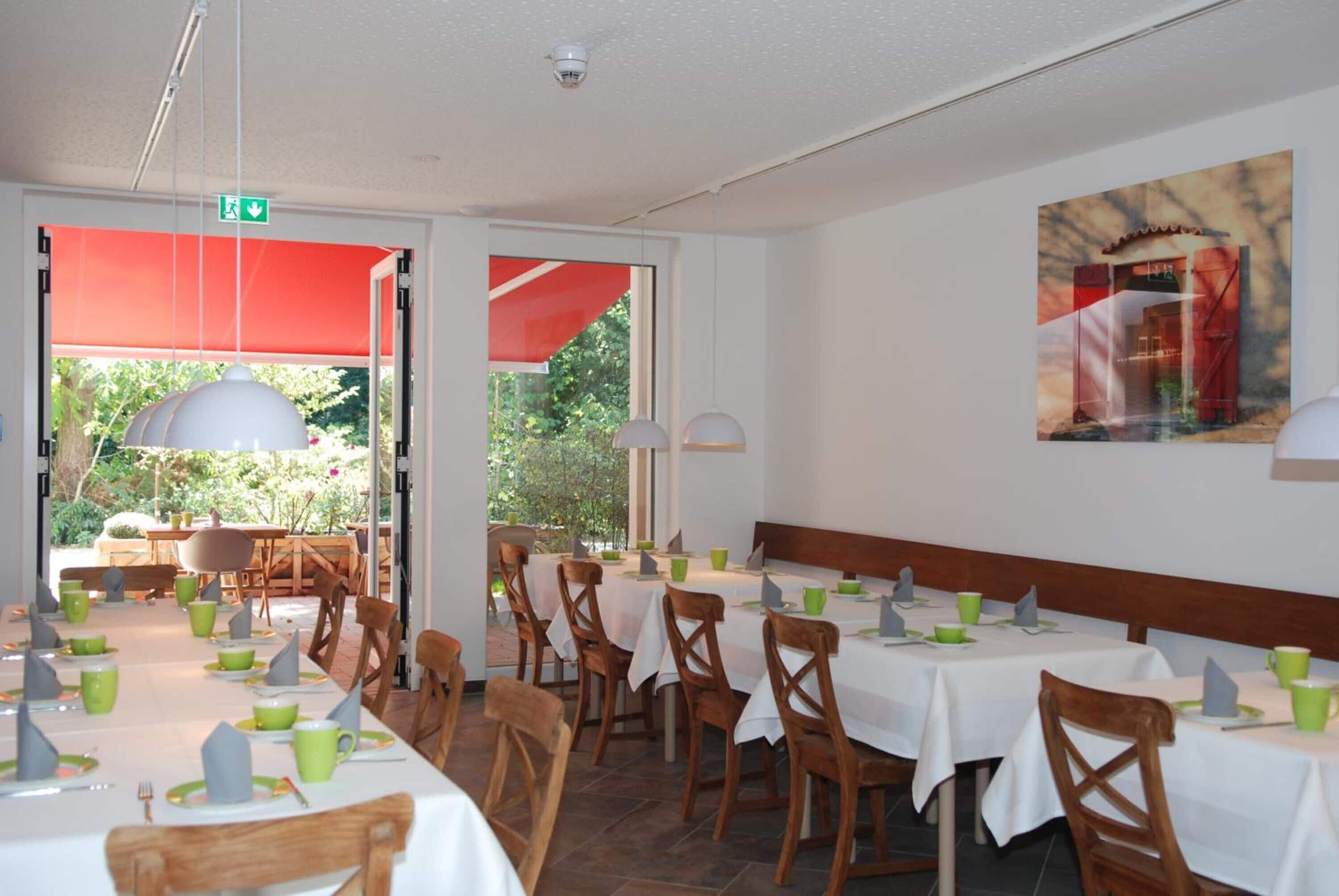 Ein Restaurant mit gedeckten Tischen, Stühlen und einem großen Fenster mit Blick ins Freie.