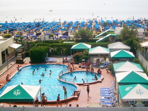 A pool area with multiple pools, lounge chairs, and umbrellas. - Hotel Caravelle & Minicaravelle (Jesolo)