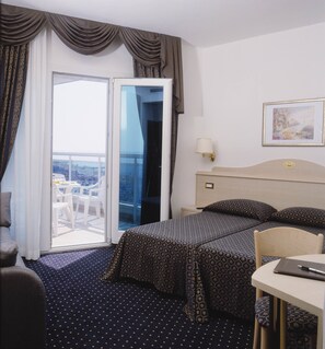 A hotel room with two beds, a balcony with a table and chairs, a painting on the wall, and a lamp. - Hotel Caravelle & Minicaravelle (Jesolo)