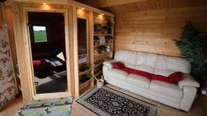 Ein gemütlicher Raum mit Holzvertäfelung, einem weißen Ledersofa, einem kleinen Bücherregal und einem Fernseher.