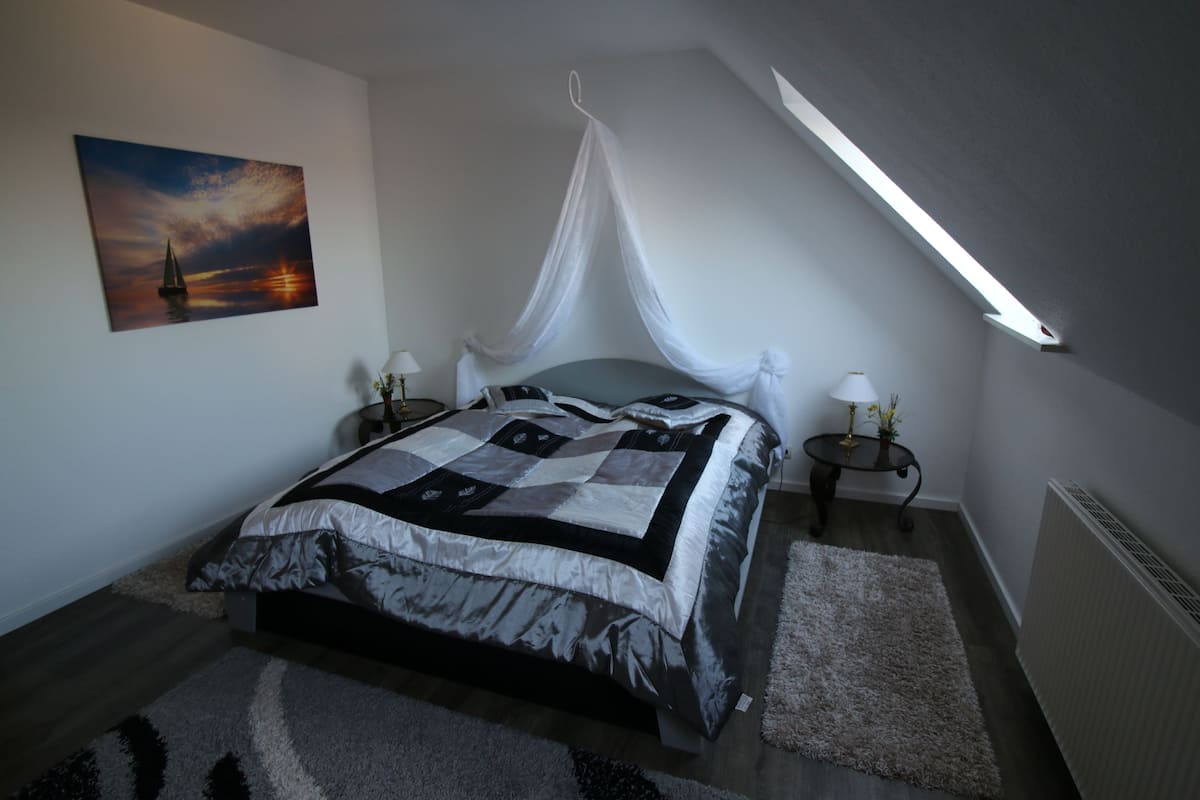 Une chambre à coucher comprenant un lit, des tables de chevet, une commode, un tableau, un baldaquin et une lucarne.