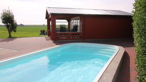 Ein rechteckiger Pool mit einem Pflasterweg, der zu einer Holzhütte mit einem Metallroof führt.