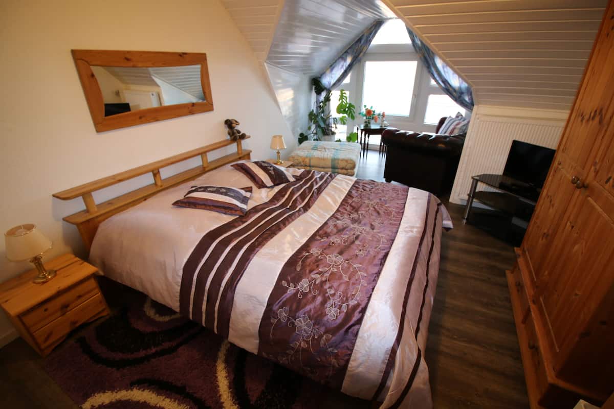 Une chambre à coucher avec un grand lit, une tête de lit en bois, une table de chevet avec une lampe, une commode et un téléviseur.