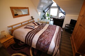 Une chambre à coucher avec un grand lit, une tête de lit en bois, une table de chevet avec une lampe, une commode et un téléviseur.