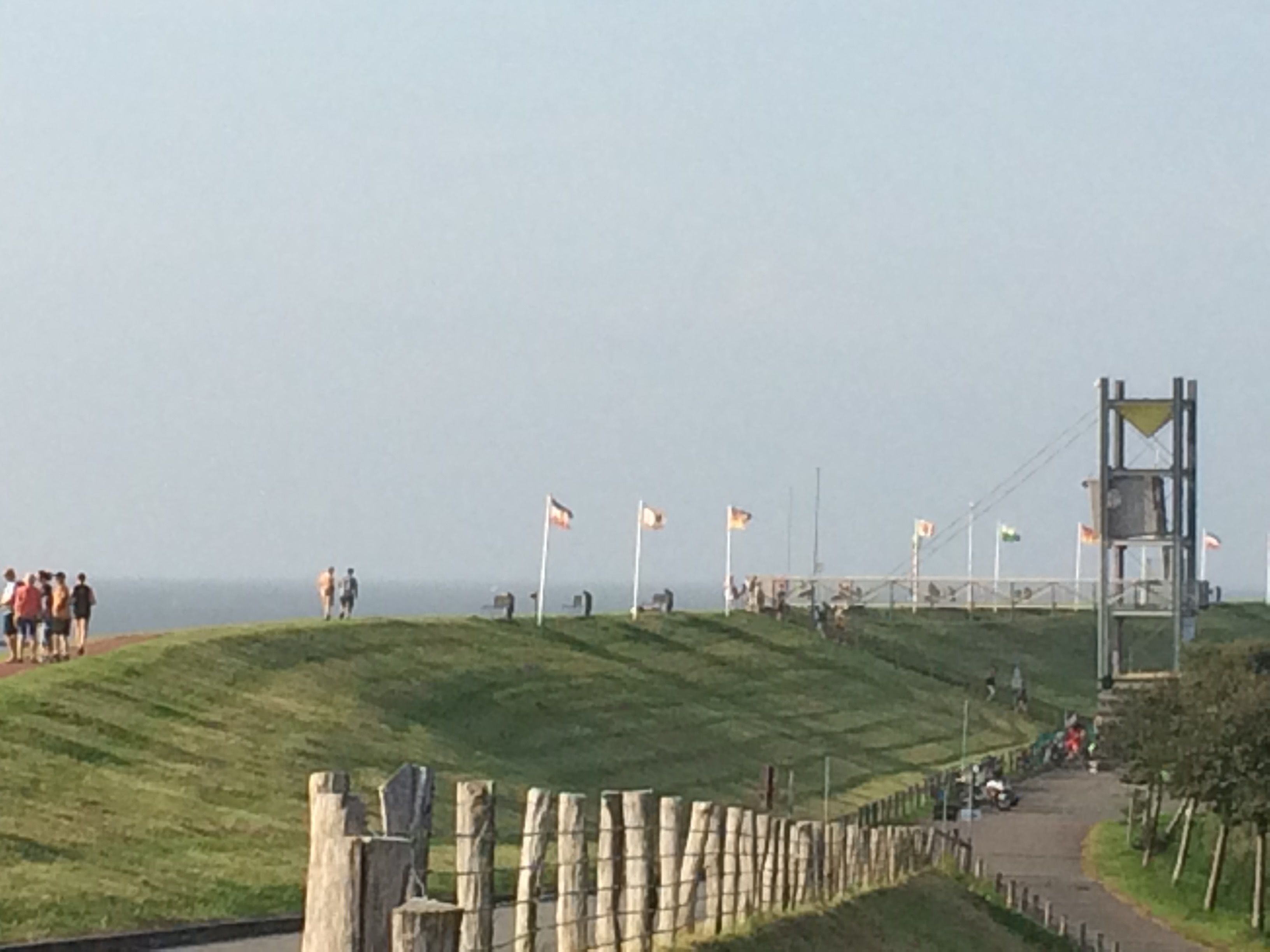 A coastal path with a wooden fence, flags, and a viewing platform.