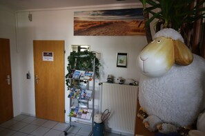 Un espace d’accueil avec un grand mouton en peluche, un panneau d’affichage où sont accrochées des brochures, et une porte portant l’inscription « Réception ».