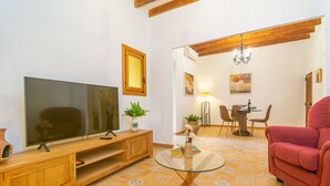 Sala de estar com televisão, móveis de madeira, mesa de centro de vidro, uma cadeira vermelha e área de jantar com cadeiras e mesa.