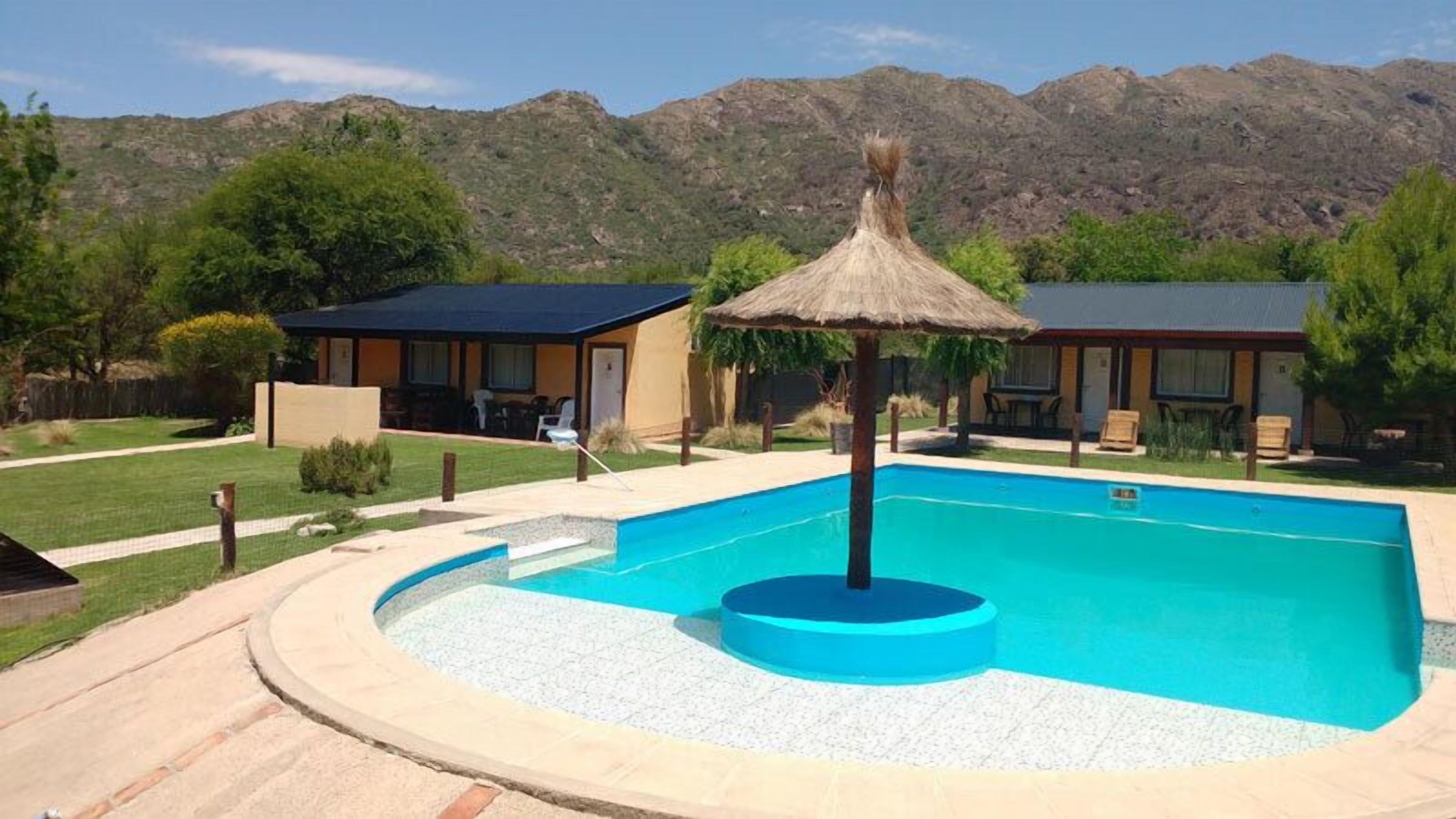 Une piscine agrémentée d’un parasol en chaume, entourée d’un espace paysager avec une chaîne de montagnes en arrière-plan.