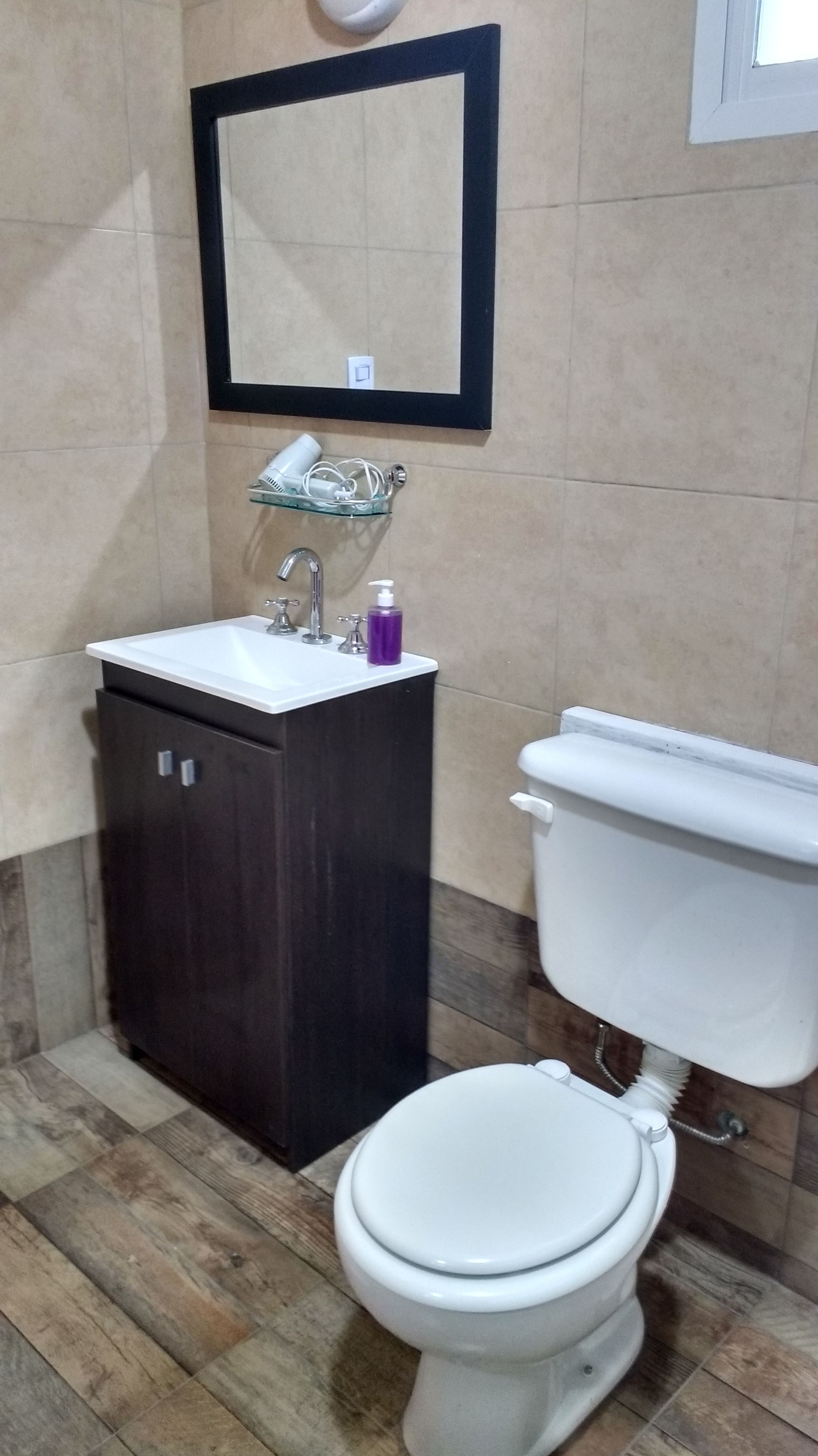 Een badkamer met een donker houten kastje, een wit wastafel, een spiegel en een wit toilet.