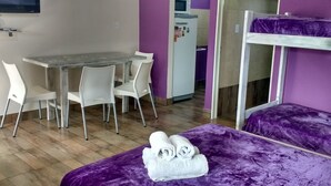 Une pièce avec une table à manger en bois, des chaises blanches, un lit violet et un lit superposé.