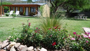 Une maison dotée d’un patio, d’un espace salon extérieur et d’un jardin agrémenté de rochers et de fleurs.