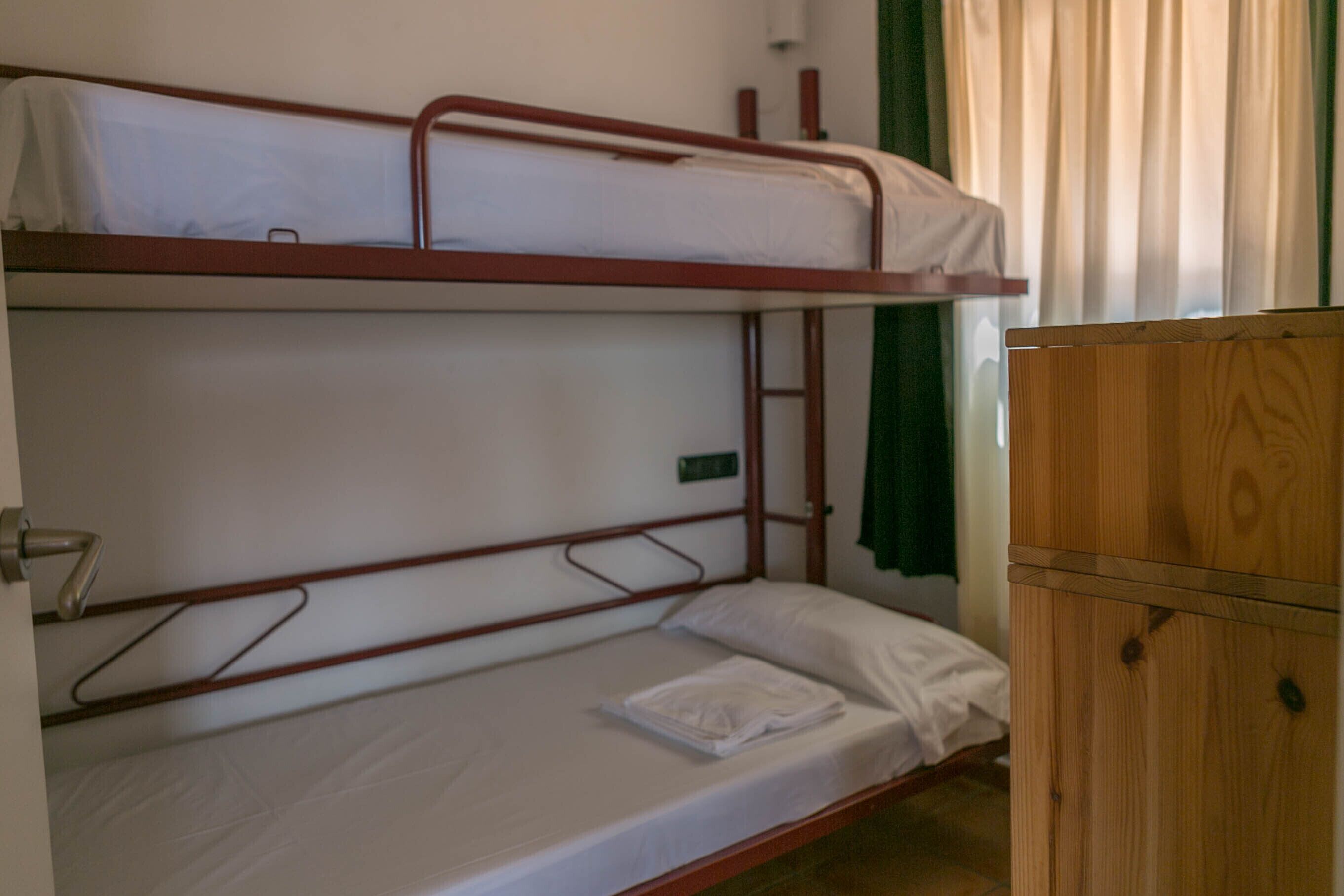 A bunk bed room with a wooden wardrobe and a green curtain.