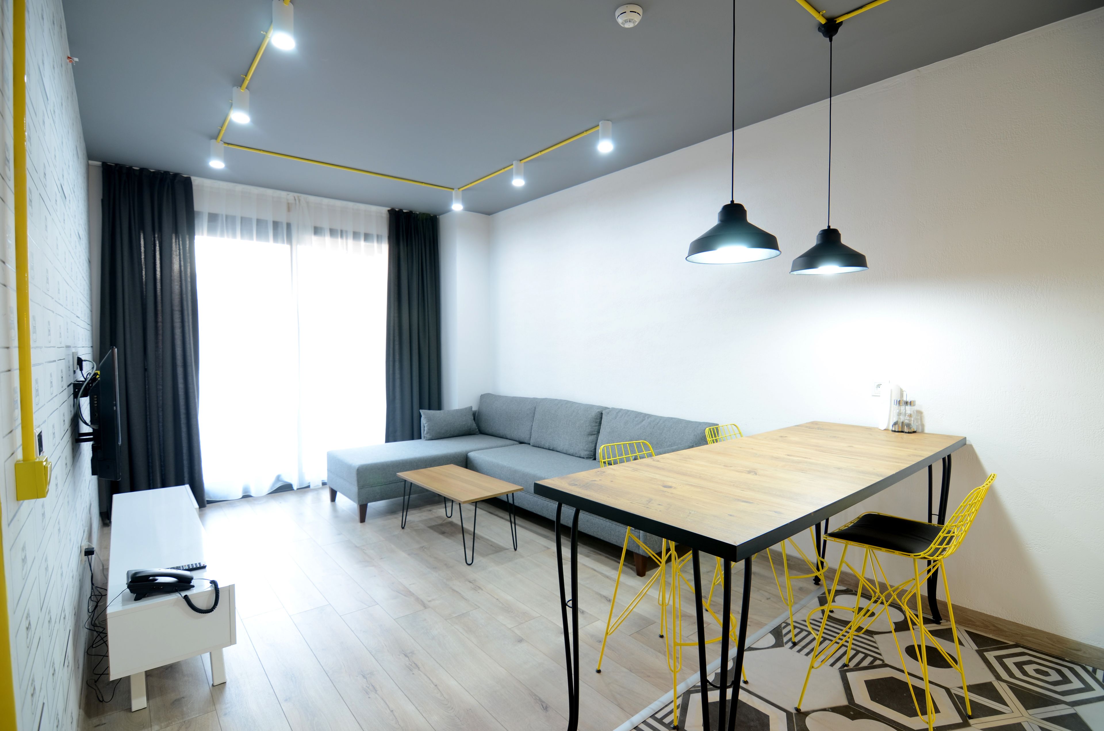 Uma sala de estar moderna com um sofá, uma mesa de jantar com cadeiras amarelas, uma pequena mesa de madeira e um armário branco.