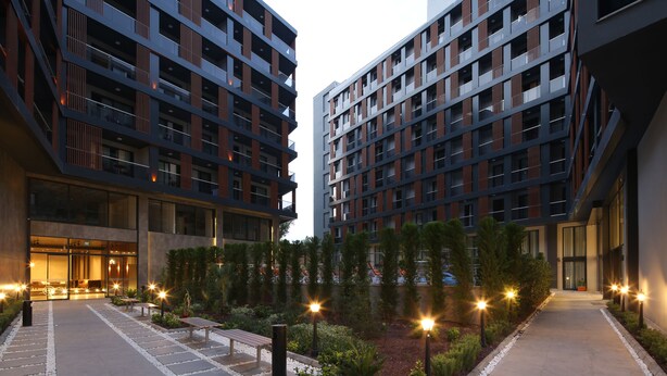 A modern building with multiple floors, large windows, and a well-lit courtyard with pathways and seating areas. - Coordinat Suits (Izmir)