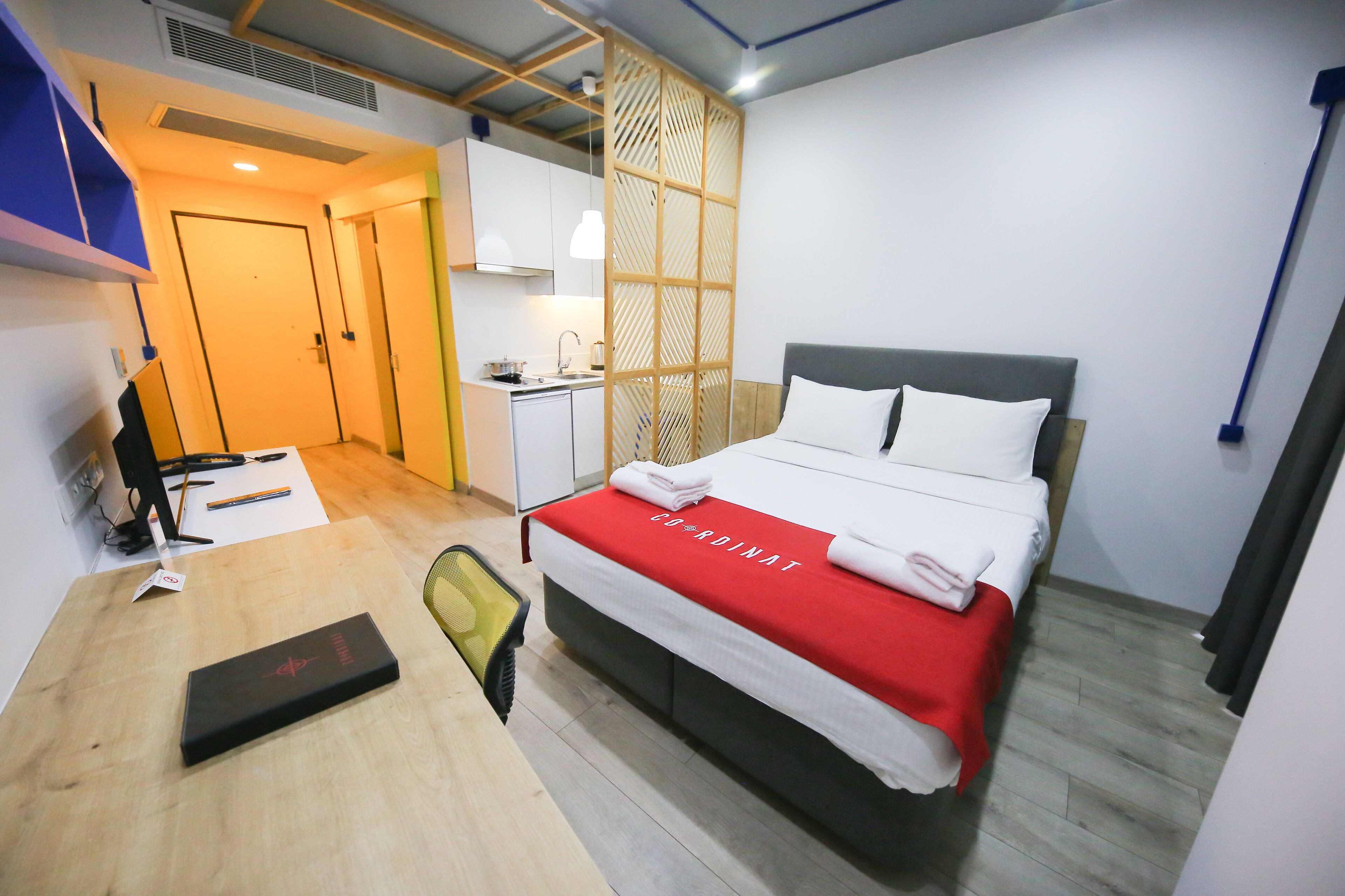 Una habitación de hotel con cama, escritorio, silla, kitchenette pequeña y baño.
