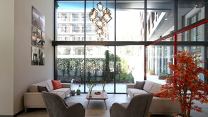 A modern living room with two sofas, a coffee table, and a large window with a view of buildings and greenery. - Coordinat Suits (Izmir)