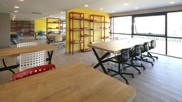 A modern library with wooden tables and chairs, red bookshelves, and large windows.