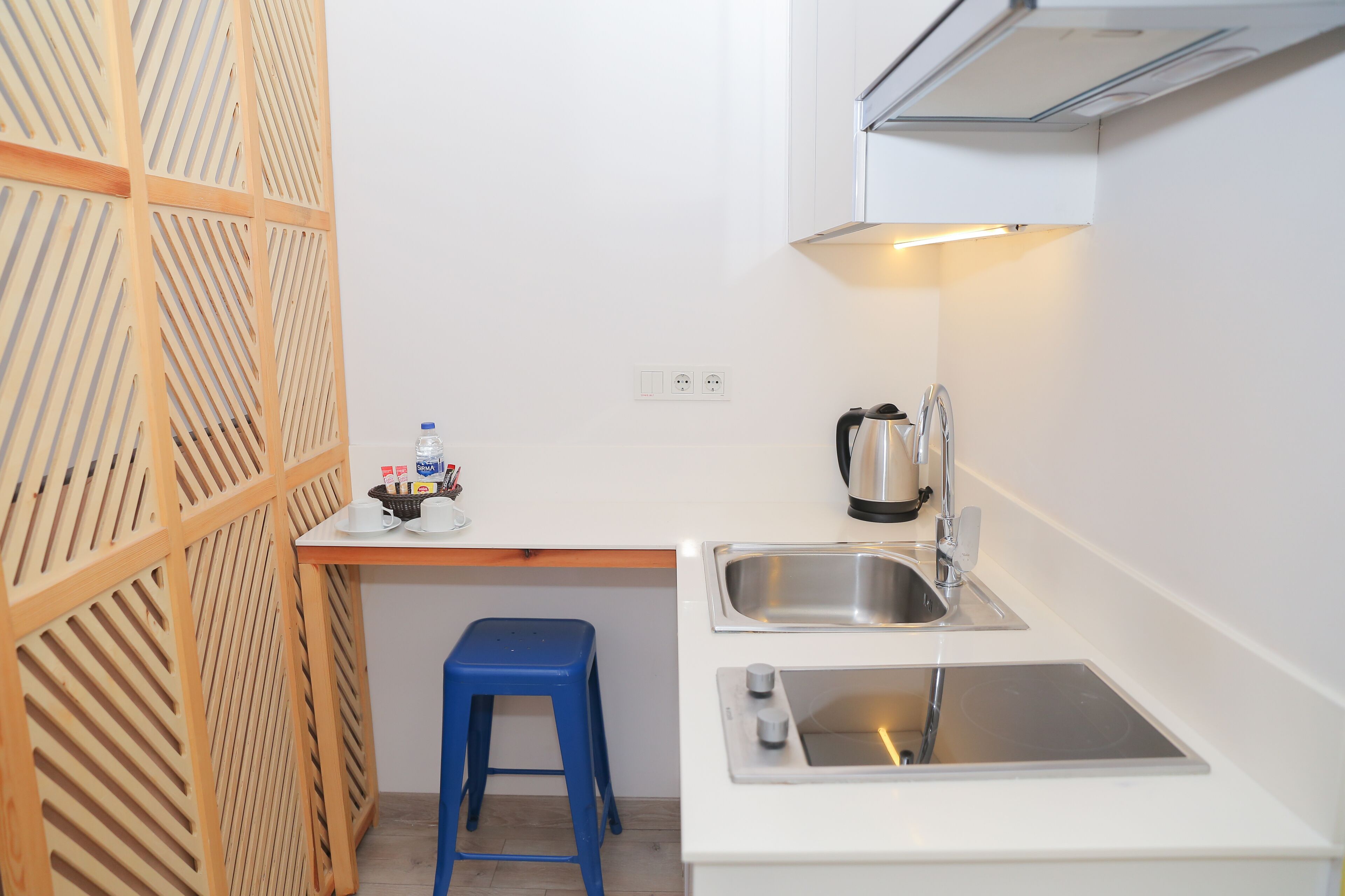 Una cocina compacta con un lavabo, una cafetera y un taburete azul.