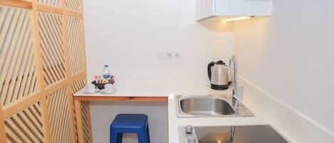 Una cocina compacta con un lavabo, una cafetera y un taburete azul.