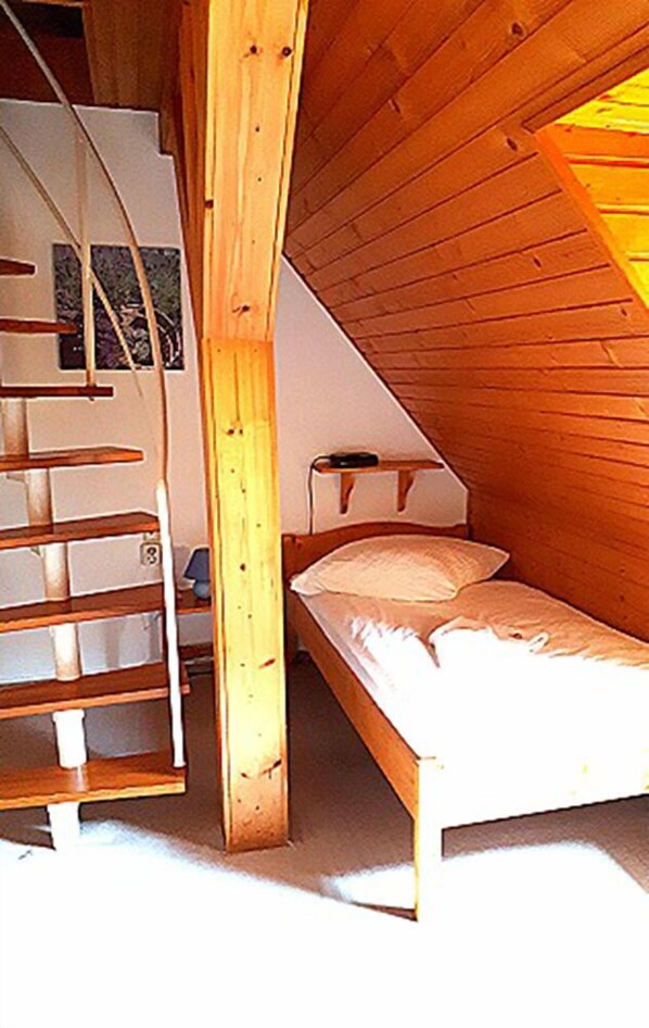 Una pequeña cabaña de una sola habitación con cama tipo altillo y escalera de madera.