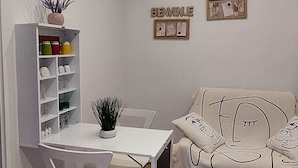 A small, well-lit room with a white desk, a chair, a sofa with a blanket, a bookshelf, and a wall clock. - independent villa, air-conditioned, ideal for couples (peschici)
