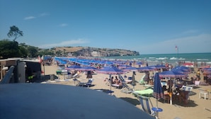 A beach with numerous blue umbrellas and sun loungers, a clear sky, and a rocky cliff in the background. - independent villa, air-conditioned, ideal for couples (peschici)