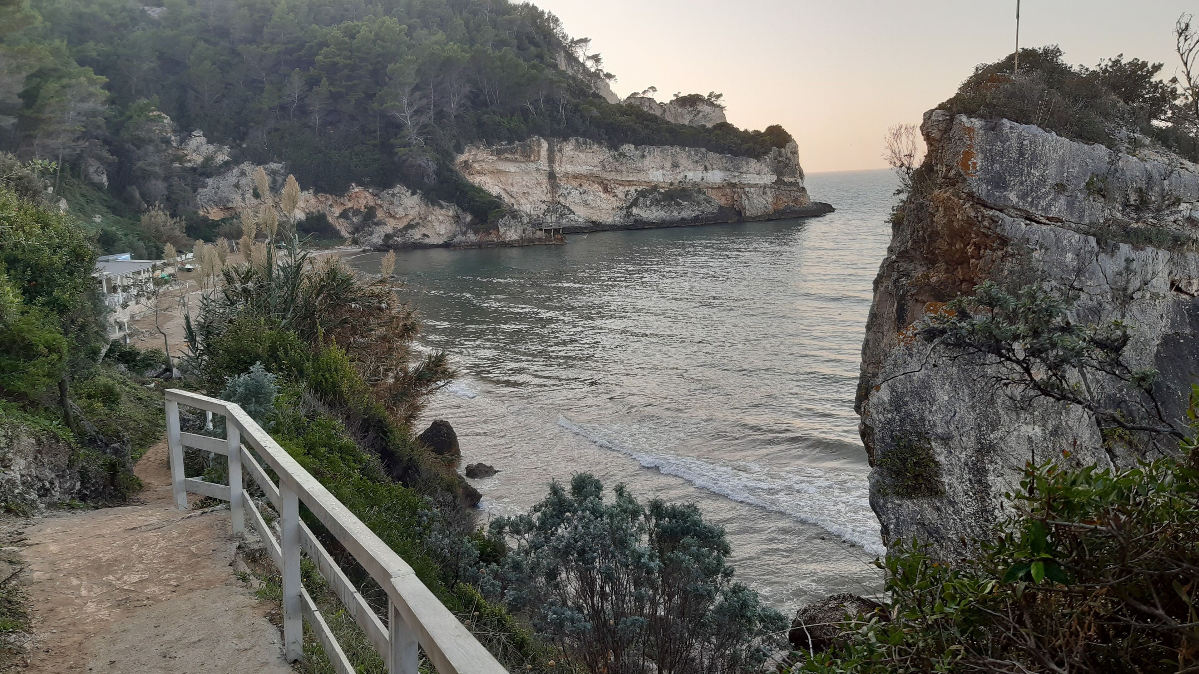 A coastal landscape with cliffs, a sea view, and a pathway leading to a building.