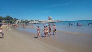 Une plage où l’on voit des gens se promener et nager, une formation rocheuse en arrière-plan et des parasols le long du rivage.
