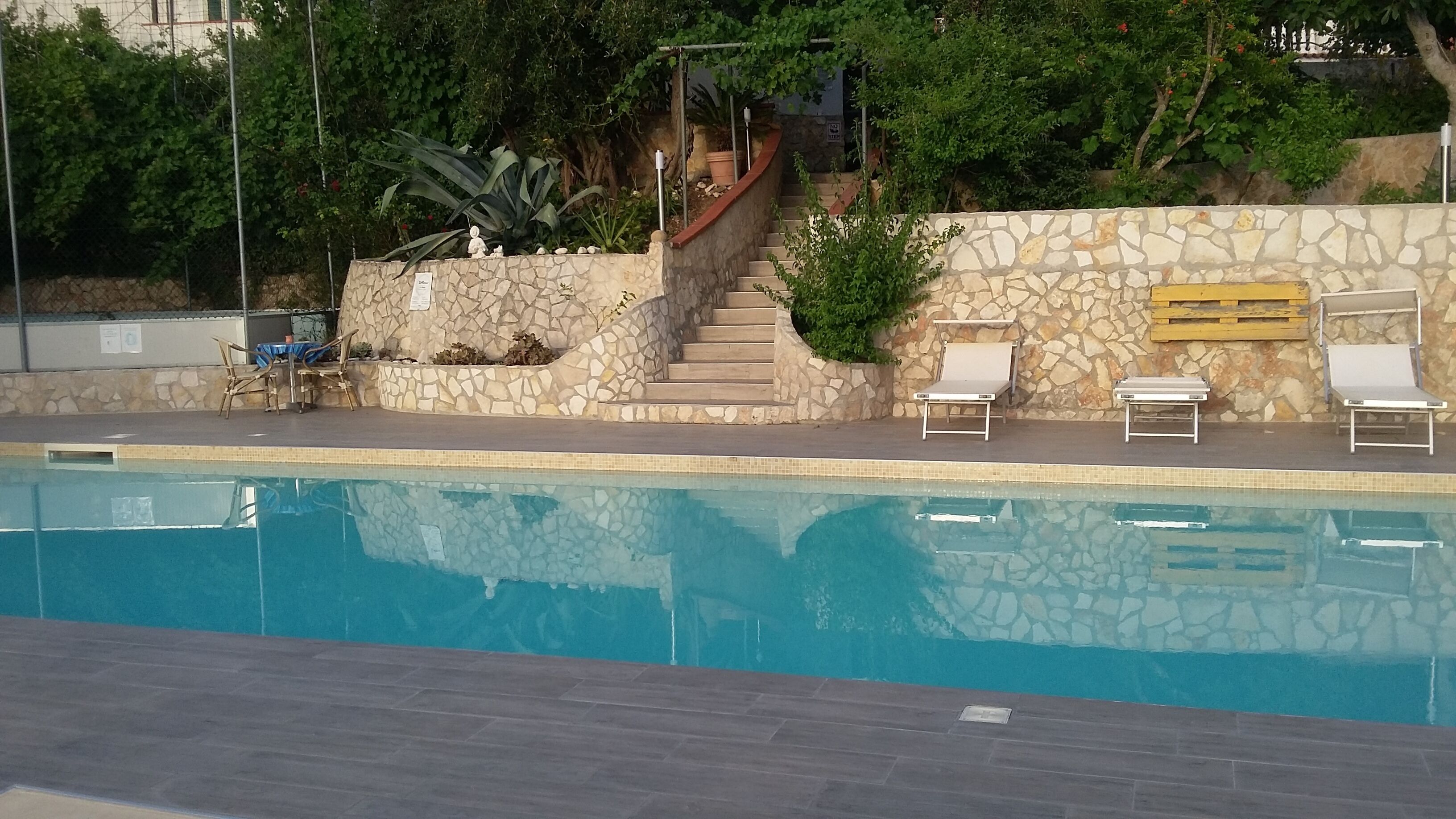 Ein Swimmingpool mit Steinstufen, die zu einer Lounge mit weißen Stühlen führen.