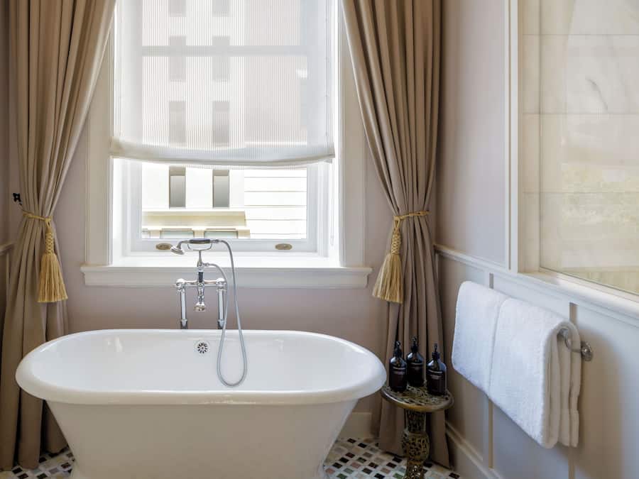 A bathroom with a freestanding bathtub, a window with curtains, and a towel rack.