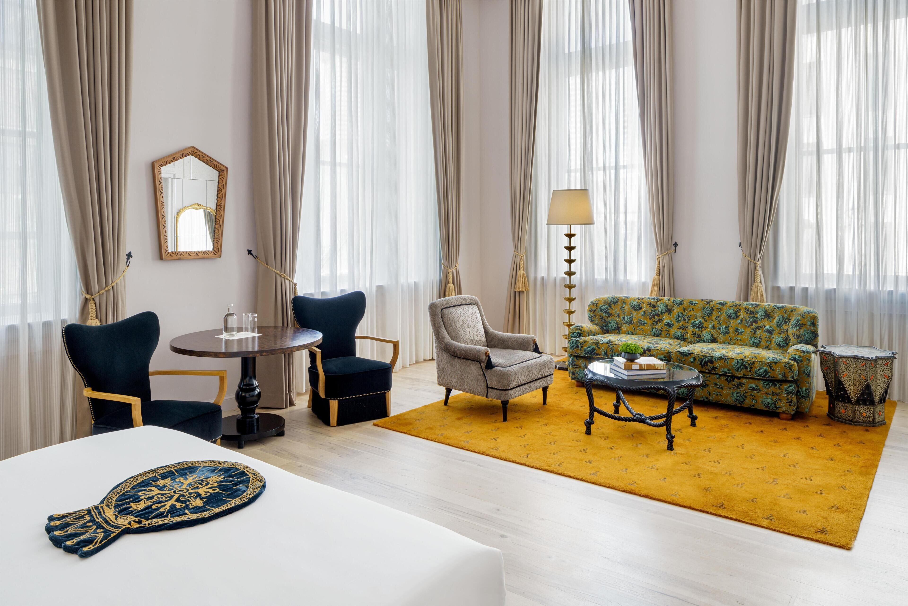 Quarto de hotel com mesa redonda, duas cadeiras, um sofá, mesa de centro e tapete estampado.