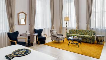Quarto de hotel com mesa redonda, duas cadeiras, um sofá, mesa de centro e tapete estampado.