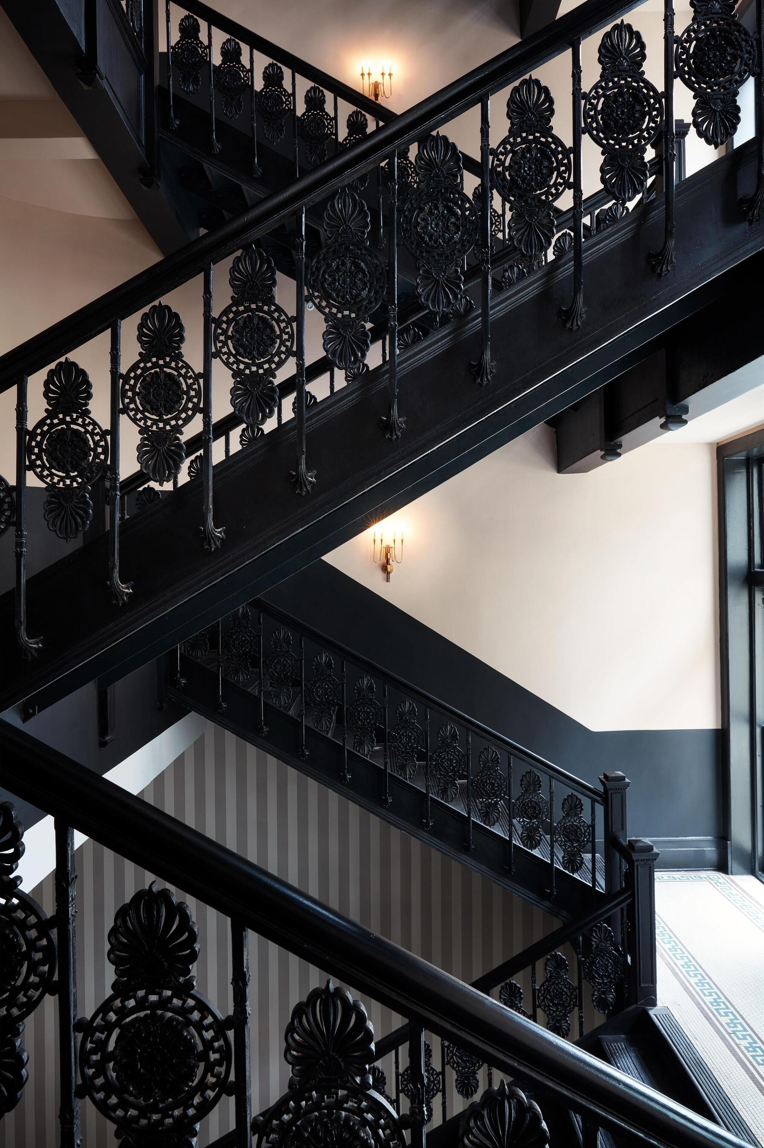 A black metal staircase with ornate railings and a wall-mounted light fixture.