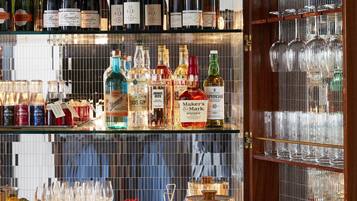 Zona de bar con estantes llenos de botellas de licores, una vitrina para copas de vino y una barra con menú y copas.