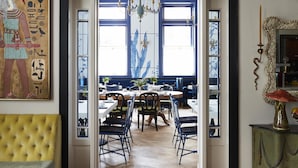 An interior with a dining area, a yellow cushioned bench, a chandelier, and a wall with Egyptian hieroglyphs. - Maison Métier, in the Unbound Collection by Hyatt (New Orleans)