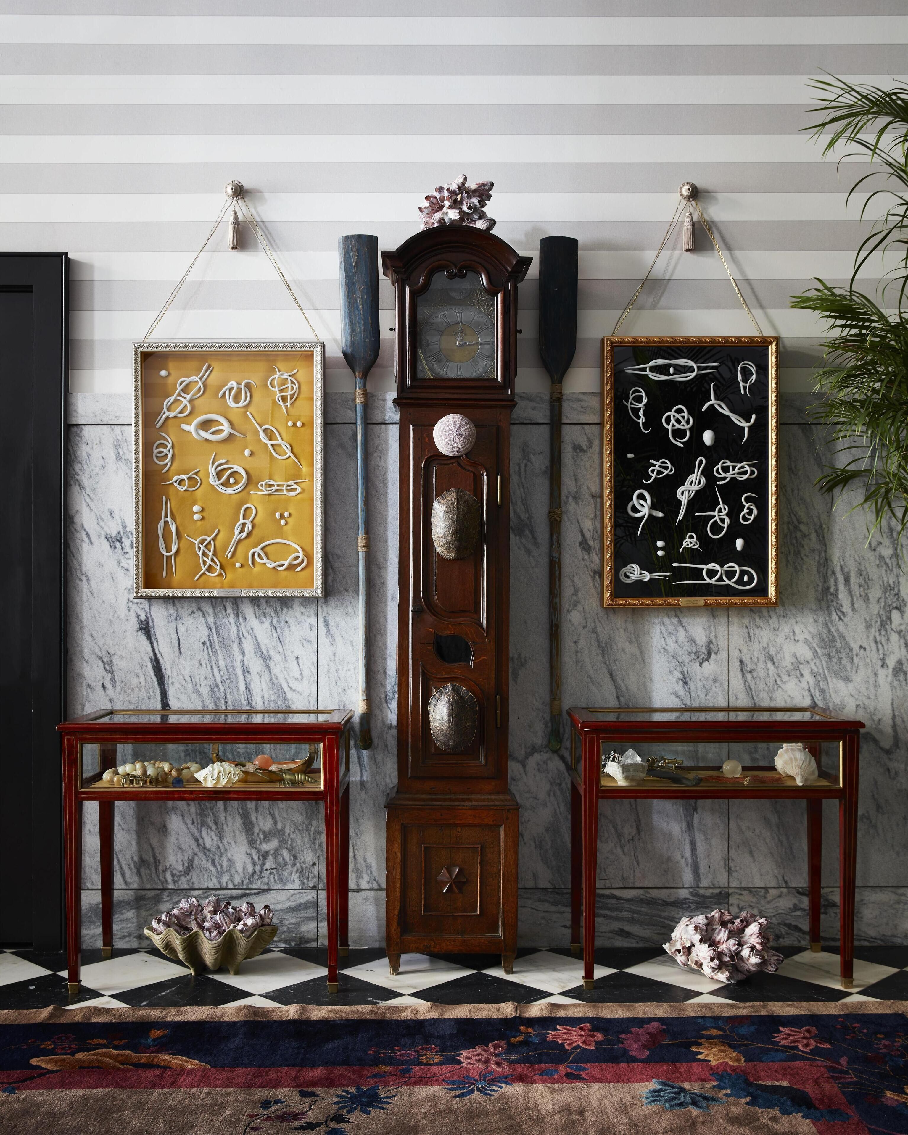 A room with a marble wall, a grandfather clock, and two framed abstract art pieces.