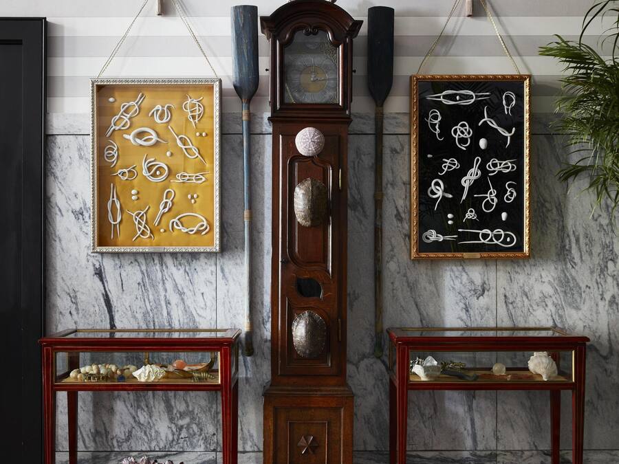 A room with a marble wall, a grandfather clock, and two framed abstract art pieces.