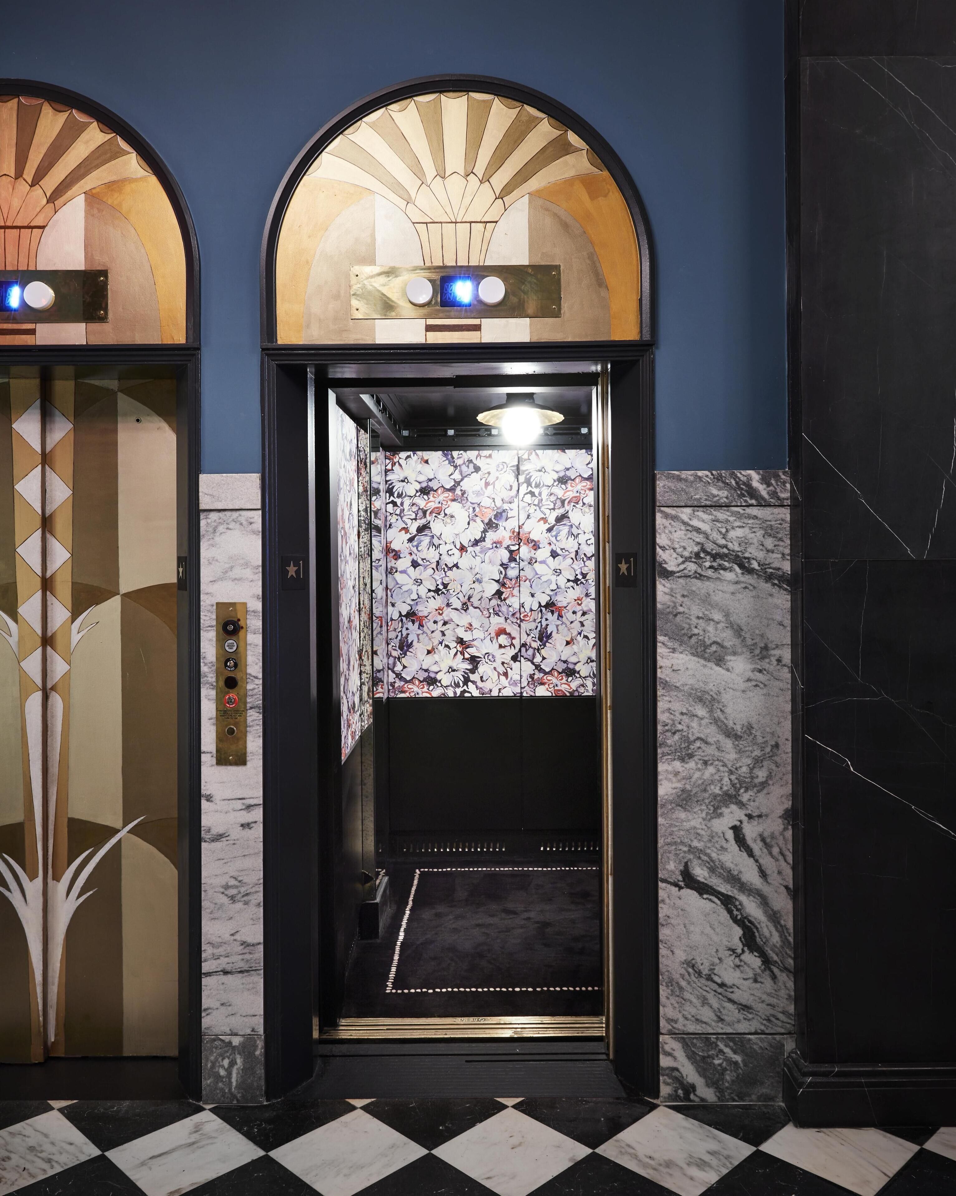 An elevator with a floral patterned wall, a black and white checkered floor, and a blue wall.
