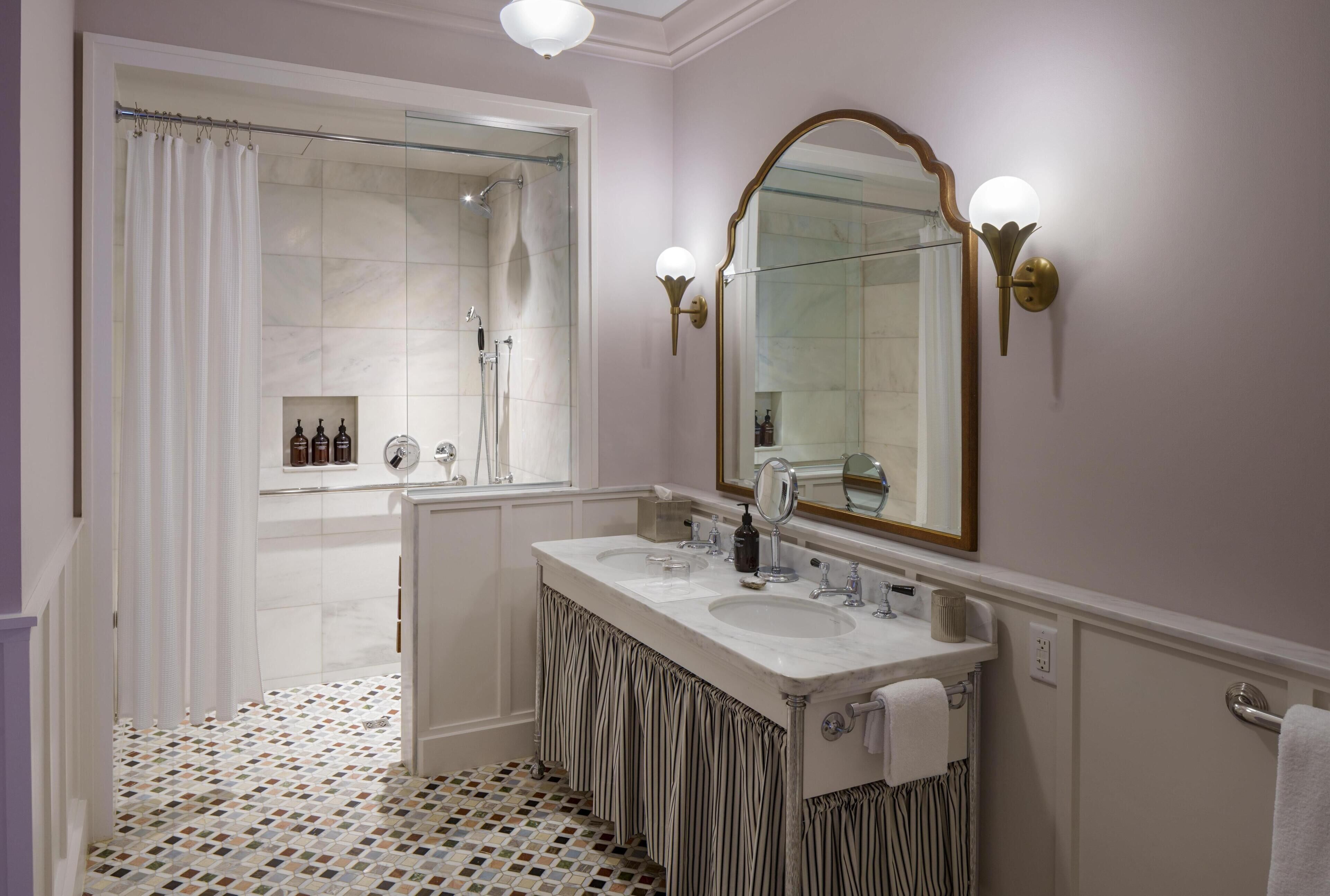 Un bagno con doccia, due lavabi, uno specchio grande e piastrelle decorative sul pavimento.