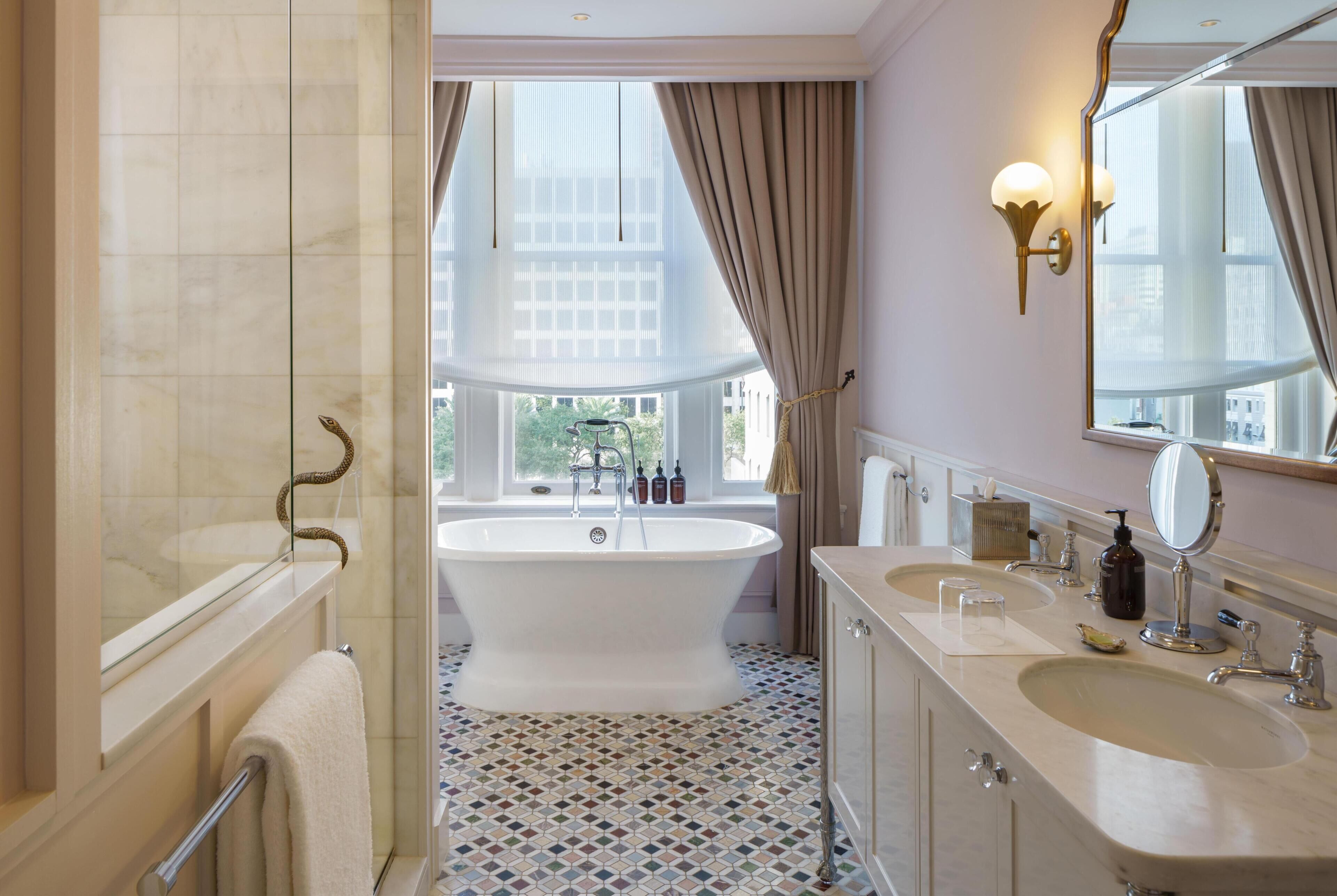 Une salle de bain avec une baignoire, deux lavabos, un grand miroir et une fenêtre avec des rideaux.