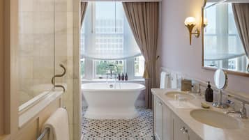 Un baño con bañera, dos lavamanos, un espejo grande y un ventanal con cortinas.