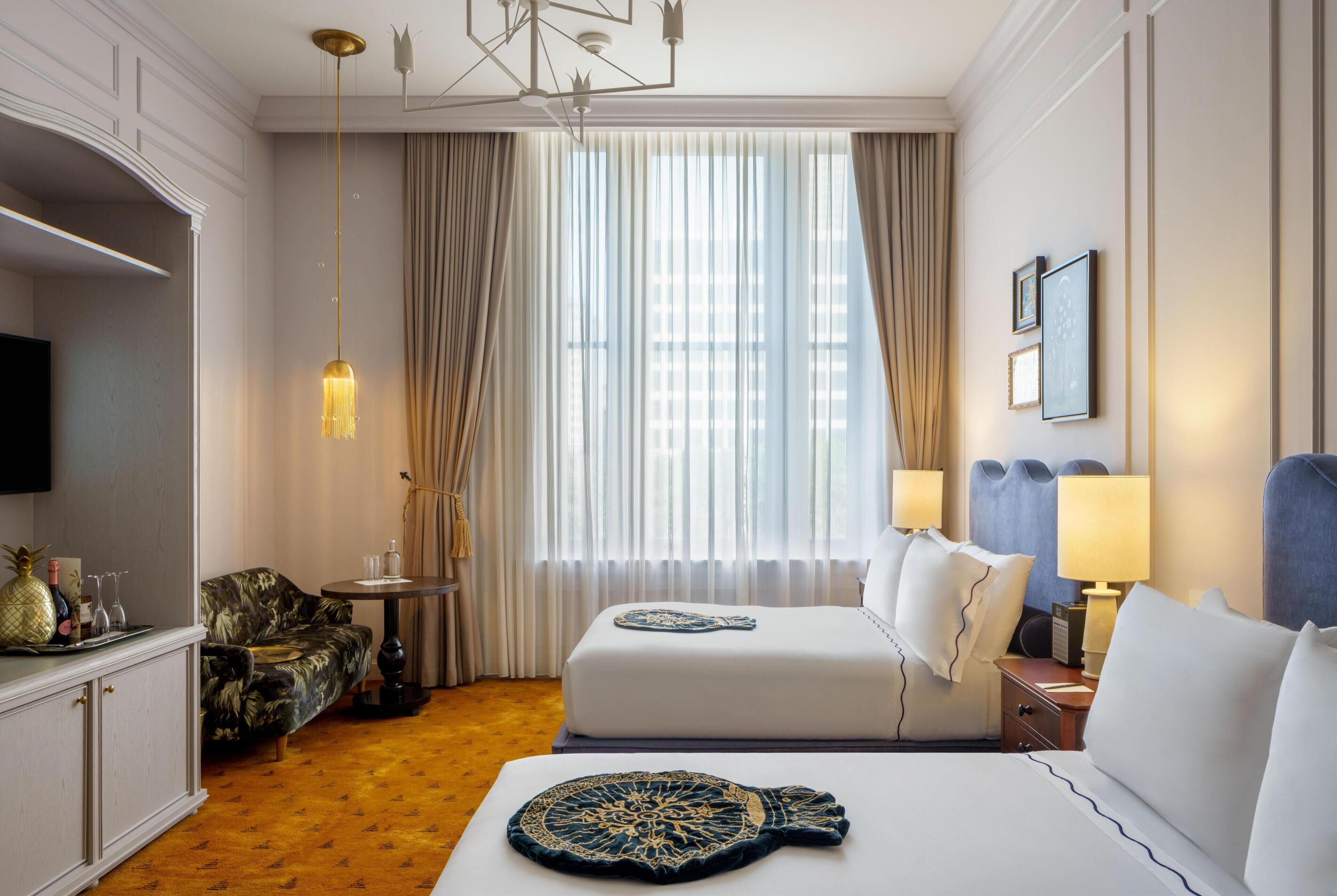 A hotel room with a bed, a chair, a small table, a TV, and a window with curtains.