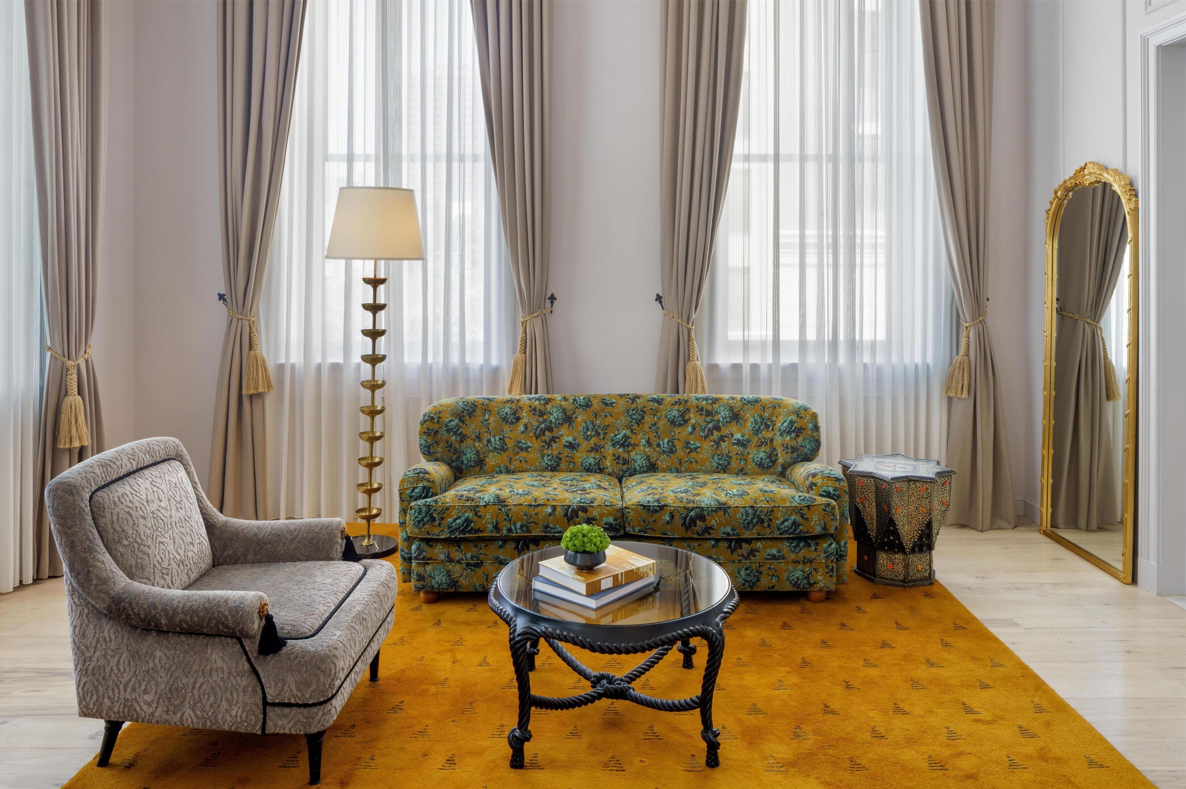 Ein Wohnzimmer mit einem gemusterten Sofa, einem gemusterten Sessel, einem runden Couchtisch, einer Lampe und einem Spiegel.