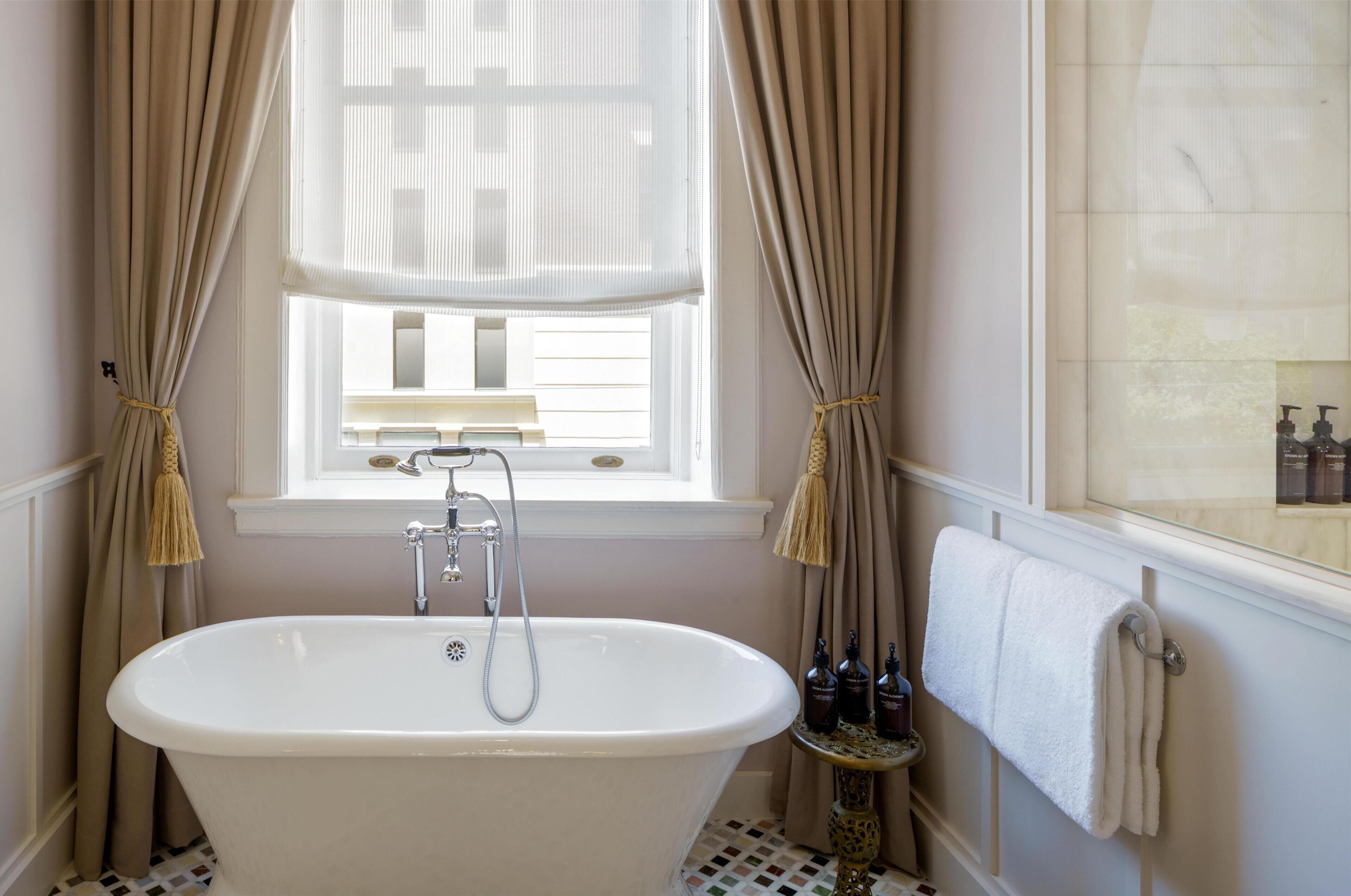 A bathroom with a freestanding bathtub, a window with curtains, and a towel rack.