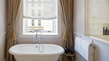 A bathroom with a freestanding bathtub, a window with curtains, and a towel rack.