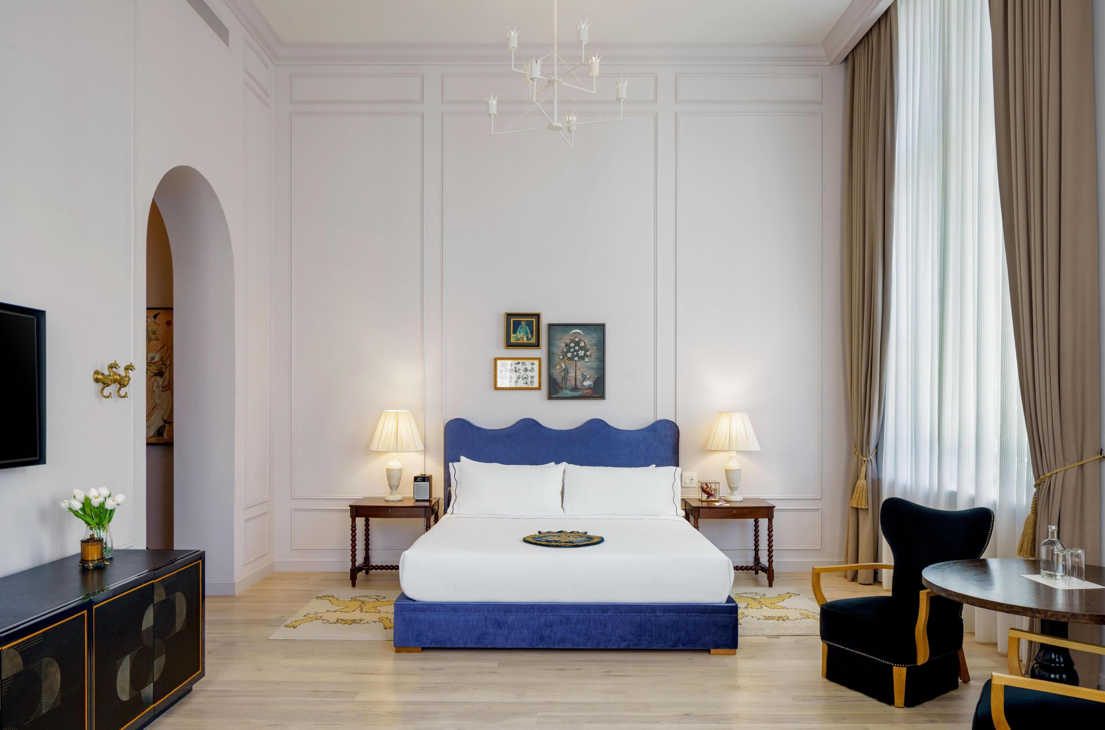 Une chambre d’hôtel avec un grand lit, deux tables de chevet avec des lampes, une télévision, une petite table ronde et une chaise.